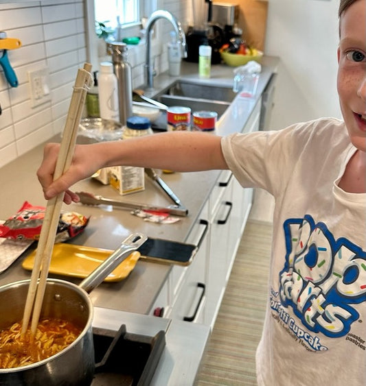 Child cooking noodles at the stove with chopsticks